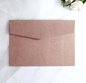 Macro detail of rose gold glitter envelope on marble surface with soft tulle and roses