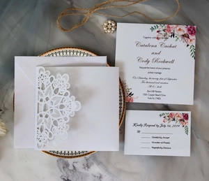 Flat lay of laser-cut wedding invitation set with floral patterns on marble background
