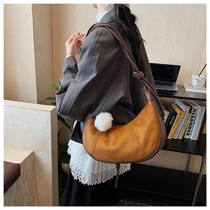 Close-up of mustard yellow suede crescent bag with dark brown knotted strap and white pom pom