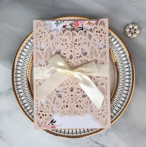 Macro shot of laser-cut wedding invitation with satin bow and floral inner card