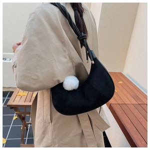 Sac hobo noir en daim avec pompon blanc porté par un mannequin en extérieur