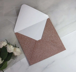 Detailed view of rose gold glitter envelope on marble surface with romantic floral accents