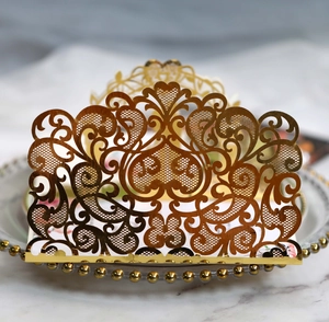 Intricate laser-cut gold metal card holder with vine patterns on a white porcelain plate
