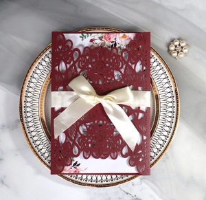 Close-up of laser-cut burgundy invitation cover with floral card and cream silk ribbon