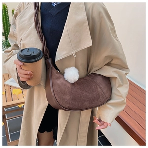 Détail d'un sac hobo en daim marron avec bandoulière tressée et charme en peluche