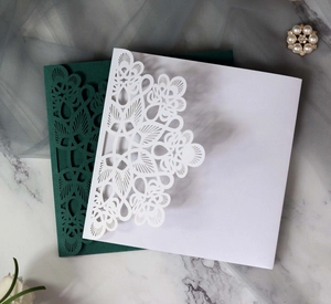 Elegant laser-cut wedding invitations in dark green and white with intricate lace floral patterns