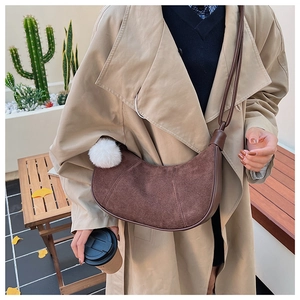 Détail d'un sac bandoulière demi-lune en daim marron avec pompon blanc sur un mannequin