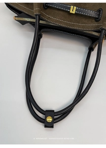 Detailed close-up of dark green suede tote with black leather handle and gold hardware