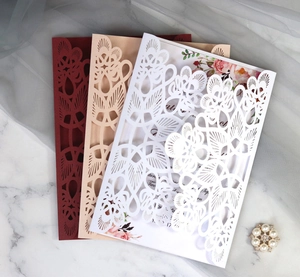 Macro detail of laser cut floral wedding invitations in burgundy, gold, and white colors