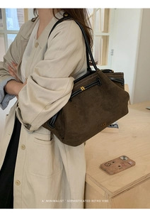 Detail of a dark brown suede tote bag with black leather straps and subtle logo branding