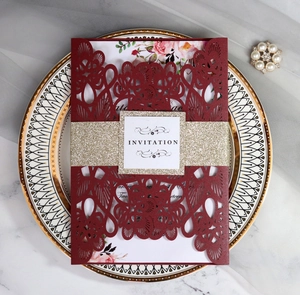 Laser cut dark red wedding invitation with gold glitter belly band on a marble surface