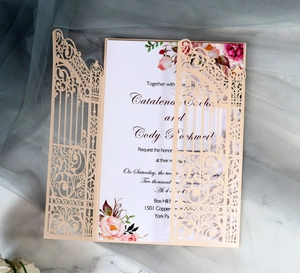Close-up of laser-cut wedding invitation with champagne gold gate and pink floral details