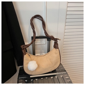 Détail du sac hobo en daim marron avec bandoulière tressée sur une valise