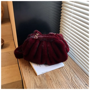 Close-up of wine red faux fur cloud bag with pleats on a book by the window