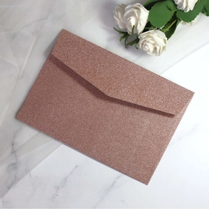 Elegant rose gold glitter envelope on white marble background with decorative white rose