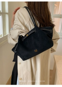 Detail of the black suede tote bag showing contrast stitching and gold logo on the shoulder