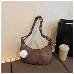 Détail du sac dumpling en daim marron foncé avec bandoulière tressée et pompon en fourrure
