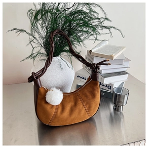 Détail du sac hobo avec poignée tressée, texture suédine et pompon blanc décoratif