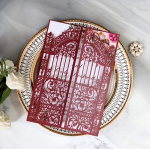 Macro shot of laser-cut burgundy wedding invitation on a golden tray with floral details