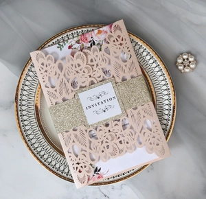 Macro detail of laser-cut floral wedding invitation with pink cover and gold glitter belt