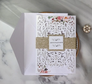 Detail of laser-cut white wedding invitation with glitter gold band on marble surface