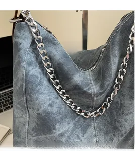 Close-up of vintage blue denim shoulder bag with rugged silver chain and white stitching