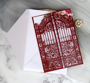 Close-up of laser-cut burgundy invitation with floral inner card and white envelope