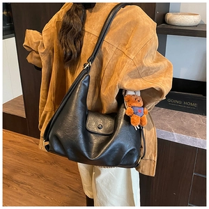 Detail of black leather crescent tote bag with an adjustable strap and brown plush bear charm