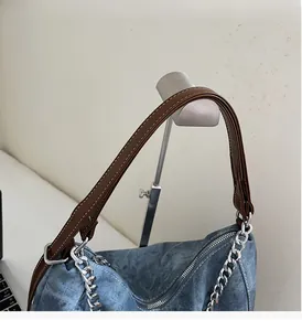 Detail of blue denim tote with brown leather handles and silver chain strap details