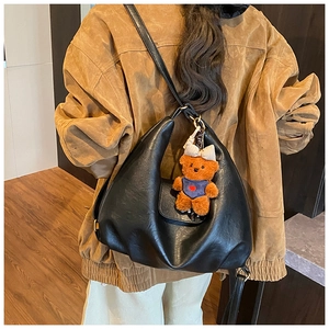 Detail of black PU leather crescent shoulder bag with a cute brown plush bear pendant
