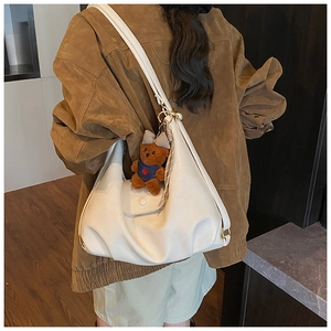 Detailed side view of a white crescent shoulder bag with a brown teddy bear pendant