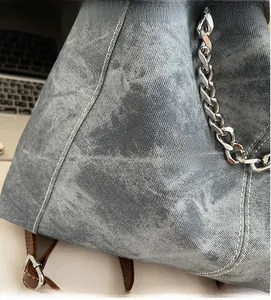 Macro detail of snow-wash denim tote bag featuring white stitching and silver chain strap