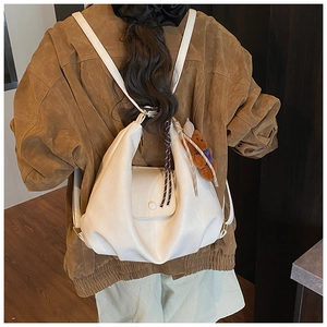 Detail of white pleated cloud backpack with brown bear charm worn on back by model