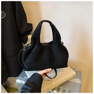 Detail of black suede pleated bucket bag with top handle and crossbody strap in a lifestyle set