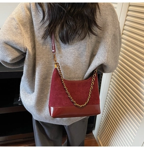 Detail view of burgundy leather dumpling bag with gold chain strap on woman's shoulder