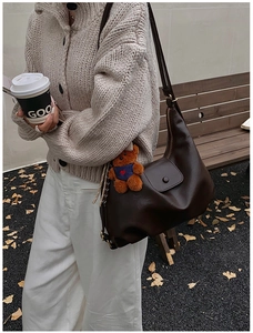 Detail of dark brown hobo shoulder bag with a cute plush bear pendant in autumn setting