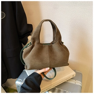 Detail of suede pleated bucket bag featuring green leather handles and gold hardware