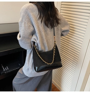 Detail of black trapezoid dumpling bag with matte leather finish and gold chain strap
