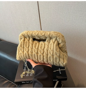 Detail of chunky cable knit bag in khaki with a slim gold chain on an art book