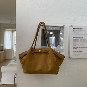 Detail of a brown suede tote bag featuring a gold buckle and brand logo on a white wall