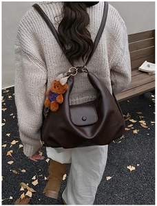 Detail of dark brown leather crescent backpack with a cute bear pendant on a park bench