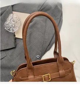 Detail view of double rounded handles and matte gold hardware on a brown leather bag