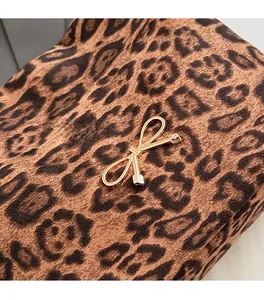 Dettaglio di un accessorio a fiocco in metallo dorato lucido per borse su tessuto leopardato