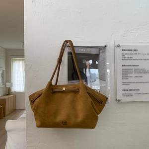 Detail of camel suede tote bag with PAN TOR logo and adjustable strap against a white wall