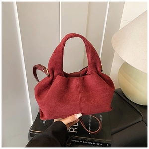 Burgundy suede hobo bag with gold adjustable buckle placed on a book in warm light