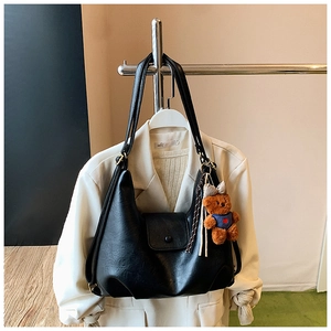 Detail view of a black pleated faux leather shoulder bag with a cute bear charm accessory