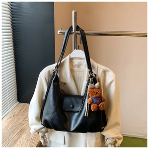 Detail of black matte leather tote bag with a cute brown plush bear charm on white blazer