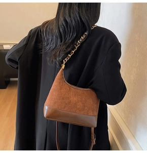 Detail of a brown suede and leather dumpling bag with a gold chain strap on a black coat