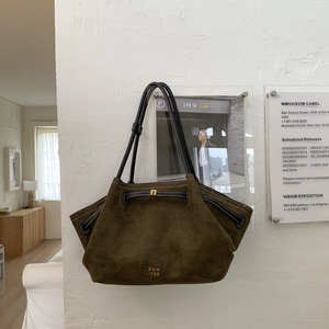 Close-up of olive green suede tote bag featuring a gold logo and black leather straps