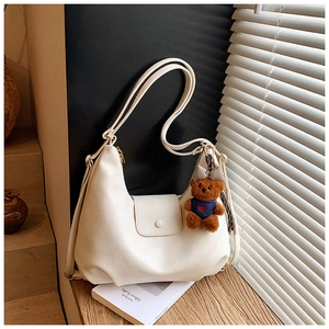 Detail of cream white faux leather shoulder bag with plush bear charm on wooden desk